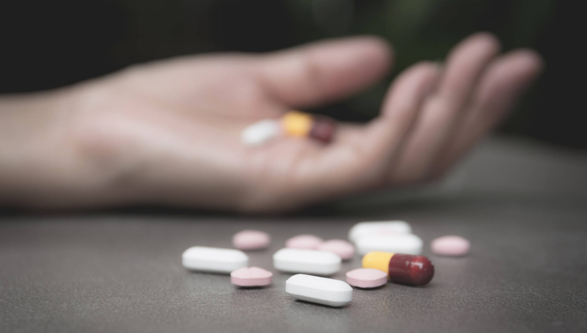 Hand holding pills with more scattered beside it
