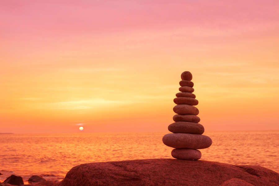 Small rocks stacked upon one another against orange sky